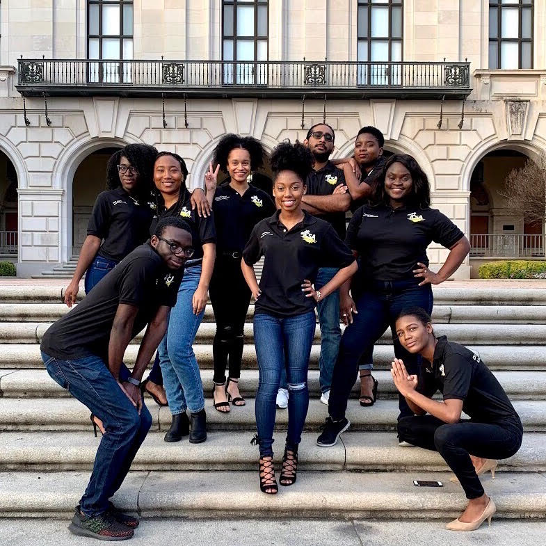 students in black shirts stand and smile in front of a staircase