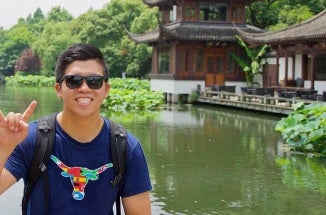 Student stands infront of a lake with the hook 'em horns hand sign and a bevo shirt