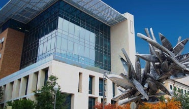 large silver clustered canoe sculpture in front of white and glass building against blue sky