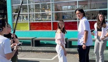 Butterfly Knot's male and female lead stand in front of Amy's Ice cream as the crew discuss the scene around them.