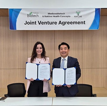 A man and woman stand holding certificates of a joint venture agreement